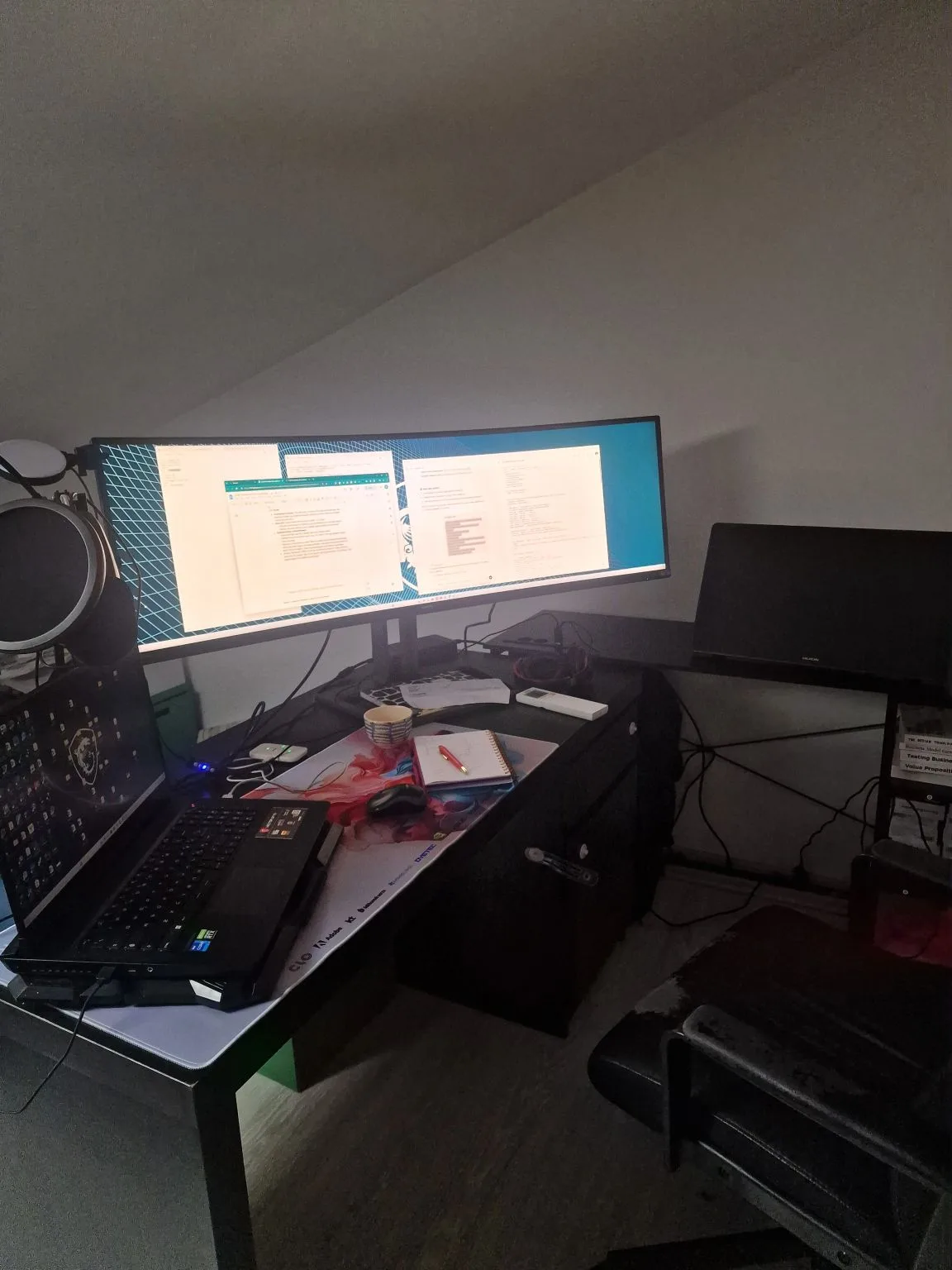 A modern home office workspace featuring a laptop, a large curved monitor displaying documents, a microphone, and a notebook, creating a productive setting ideal for tasks like fashionINSTA AI analysis.